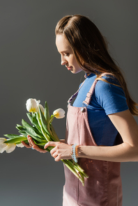side view of woman holding blooming tulips isolated on grey