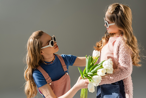 mother in sunglasses receiving flowers from happy daughter isolated on grey