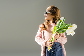 happy kid in sunglasses holding flowers isolated on grey
