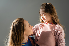 cheerful mother and daughter looking at each other isolated on grey