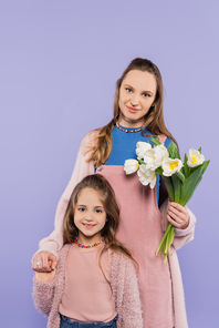 happy woman holding tulips near daughter isolated on purple