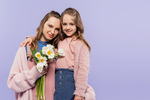 happy woman holding tulips near smiling daughter isolated on purple