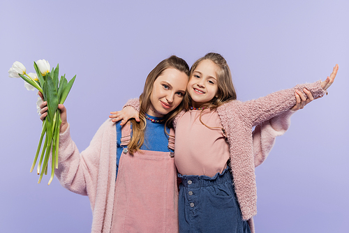 woman holding tulips near smiling daughter with outstretched hand isolated on purple