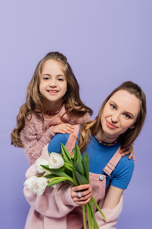 smiling woman holding tulips near happy daughter isolated on purple