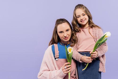 pleased mother and daughter holding tulips isolated on purple