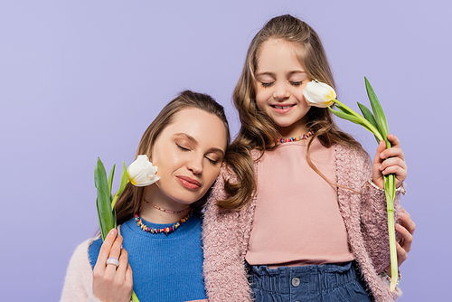 pleased mother and daughter with closed eyes holding tulips isolated on purple