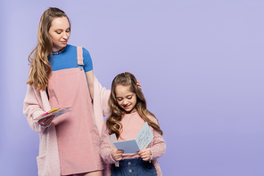 cheerful kid reading greeting card to mother isolated on purple