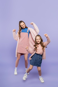 full length of happy mother in pink overall dress dancing with joyful girl on purple