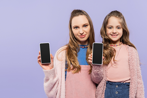 happy mother and daughter showing smartphones with blank screen isolated on purple