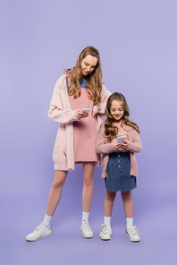 full length of mother and daughter using gadgets on purple