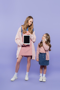 full length of woman showing digital tablet with blank screen near kid talking on smartphone on purple