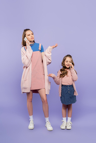 full length of mother and daughter talking on mobile phones while gesturing on purple
