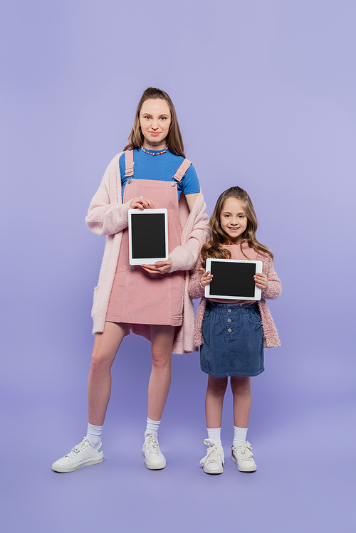 full length of mother and daughter holding digital tablets with blank screen on purple