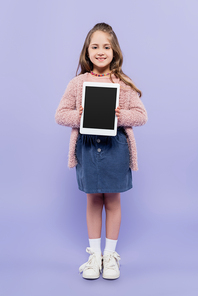 full length of cheerful girl holding digital tablet with blank screen on purple