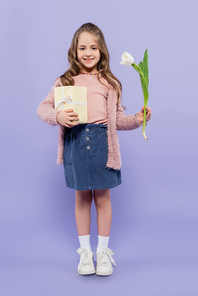 full length of happy girl holding gift box and tulip on purple
