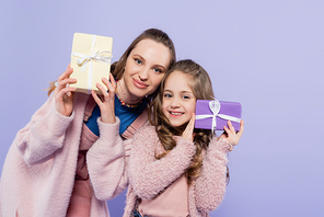 happy kid and cheerful mother holding presents isolated on purple