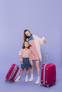 full length of happy mother and child taking selfie near baggage on purple