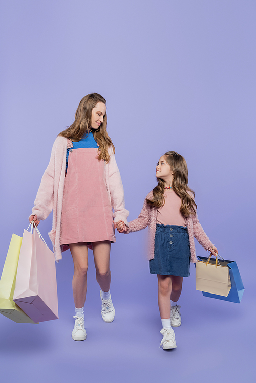 full length of mother and daughter holding shopping bags while walking on purple
