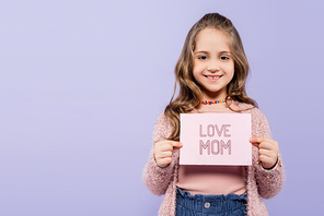 happy kid holding greeting card with love mom lettering isolated on purple