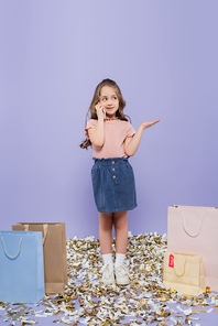 full length of girl talking on mobile phone near shopping bags and gesturing on purple