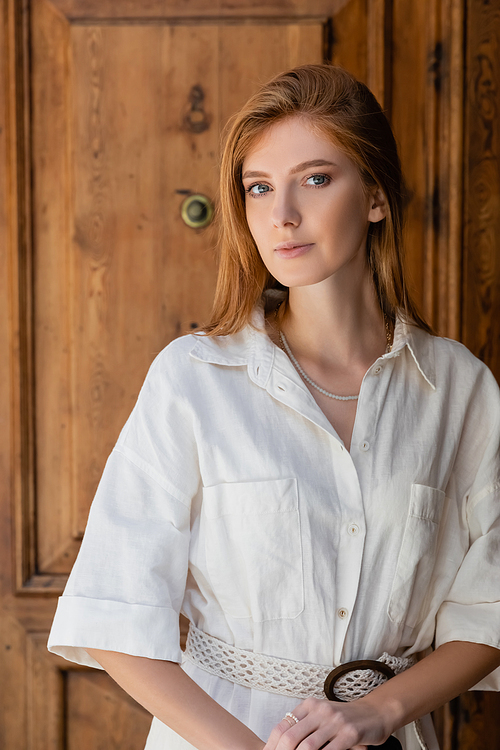 portrait of young redhead woman looking at camera near wooden door