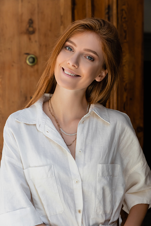 portrait of smiling redhead woman looking at camera near wooden door