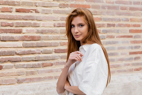 portrait of redhead woman in dress posing near brick wall on european street