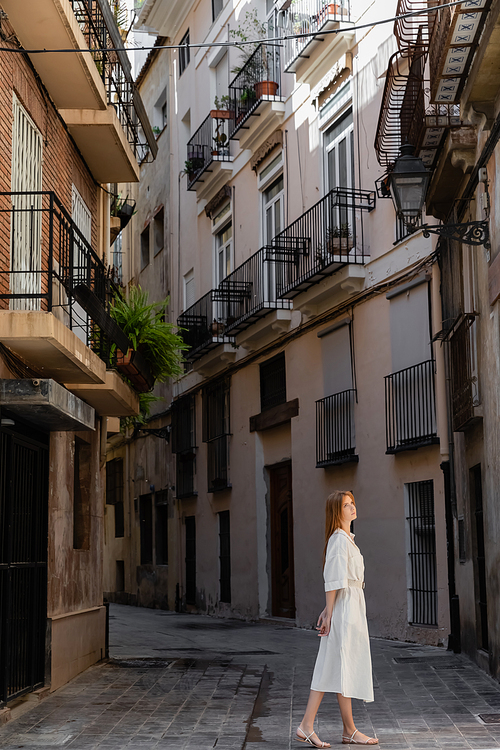 redhead woman in dress standing near houses on european street in valencia