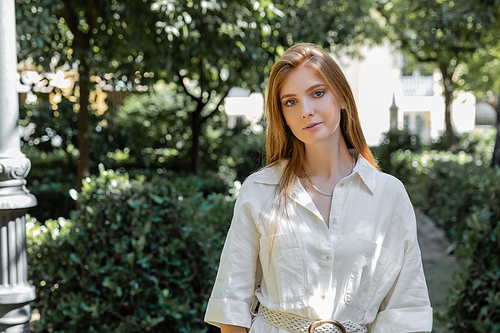 portrait of young and redhead woman in dress looking at camera in green park in valencia