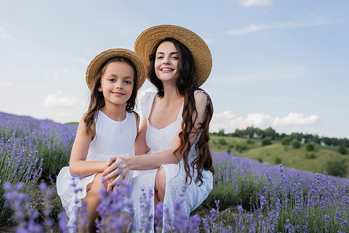 cheerful mom and daughter sitting in lavender field and looking at camera
