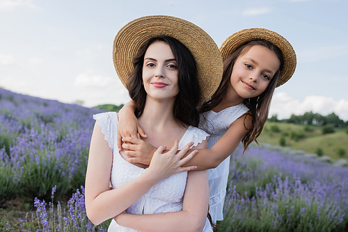 happy girl in straw hat hugging mother in blurred field