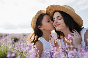 child kissing woman smiling with closed eyes in flowering field