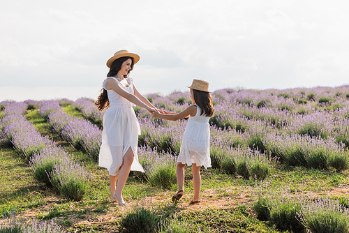 happy woman and girl in straw hats dancing in lavender meadow