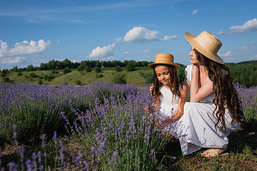 woman and child in straw hats and white dresses near blooming lavender in meadow