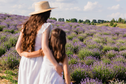 back view of blurred mother and daughter in straw hats hugging in lavender field
