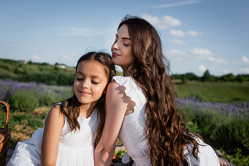 woman and child with long hair and closed eyes sitting in blurred meadow