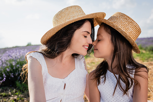 cheerful mother and daughter in straw hats smiling with closed eyes outdoors