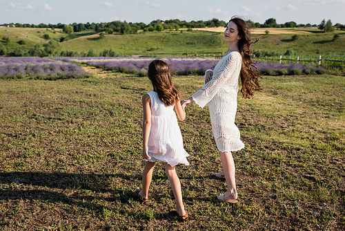 happy pregnant woman holding hands with daughter while walking in field