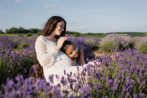 happy pregnant woman with daughter embracing in blurred lavender meadow