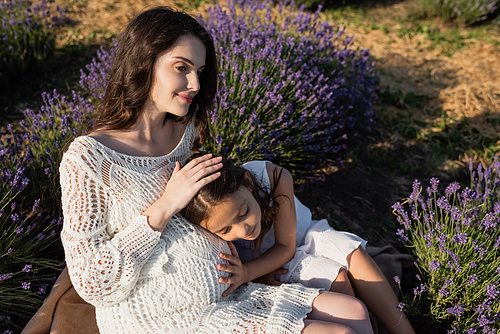 high angle view of smiling pregnant woman with child sitting in blooming field