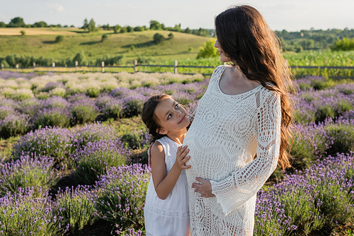 cheerful child embracing pregnant mom in field with blossoming lavender