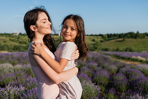 brunette woman embracing daughter smiling at camera in lavender meadow