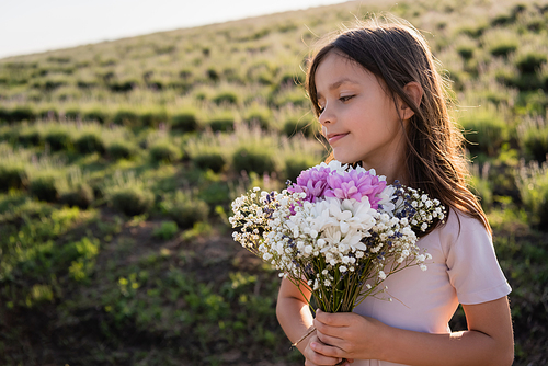 smiling woman with long hair holding bouquet of flowers in summer field