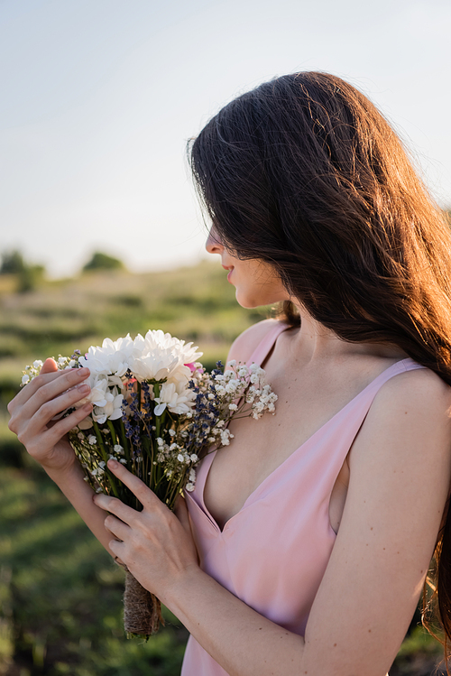 brunette woman with long hair holding bouquet of summer flowers