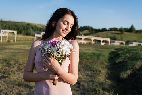 pretty brunette woman smiling and holding bouquet of summer flowers