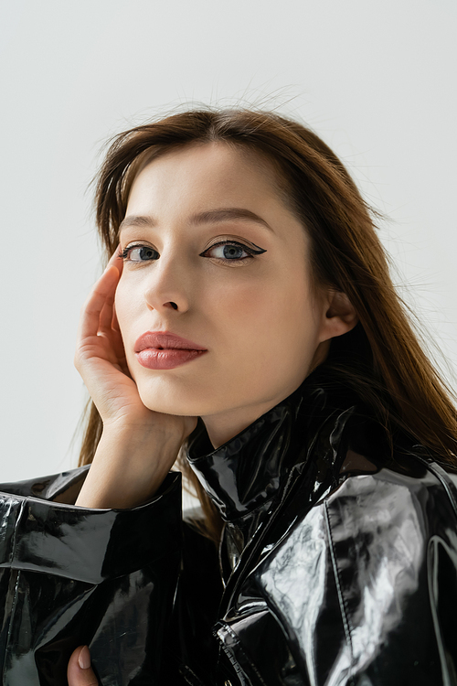 portrait of young woman in black latex jacket looking at camera isolated on grey