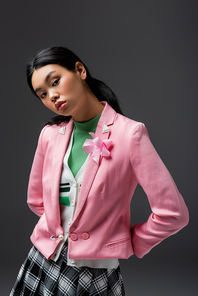 Trendy young asian model in pink jacket looking at camera isolated on grey