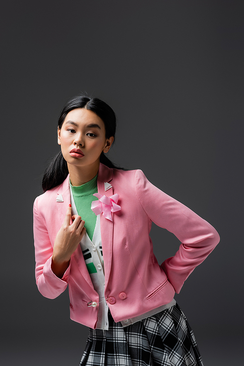 Stylish asian woman in pink jacket posing isolated on grey