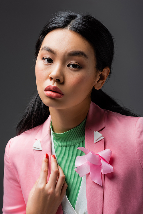 Portrait of asian woman in pink jacket looking at camera isolated on grey