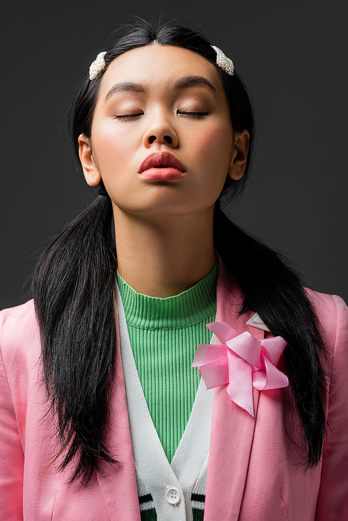 Portrait of stylish asian model in jacket closing eyes isolated on grey